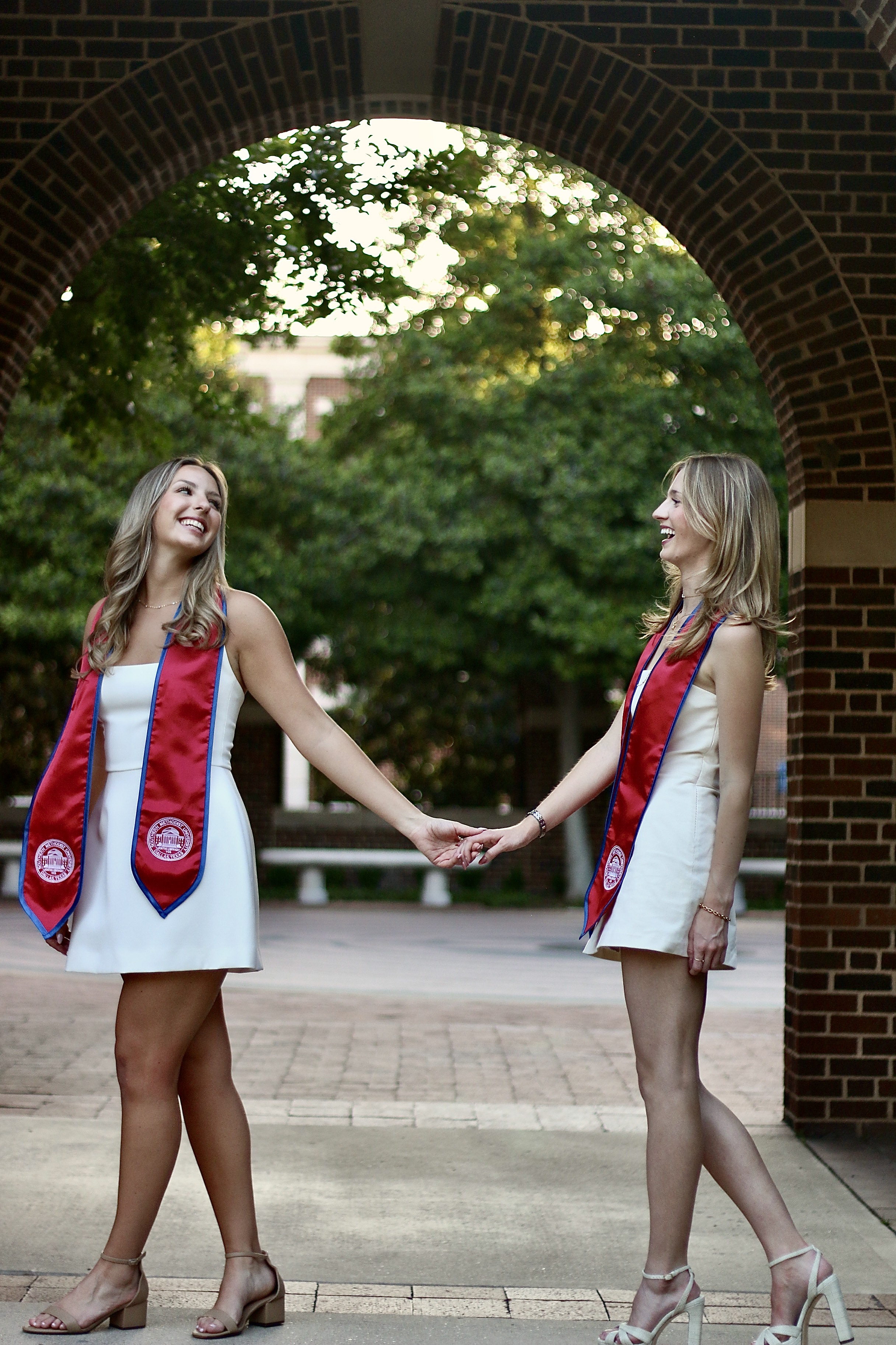 Two graduates holding hands under an arch