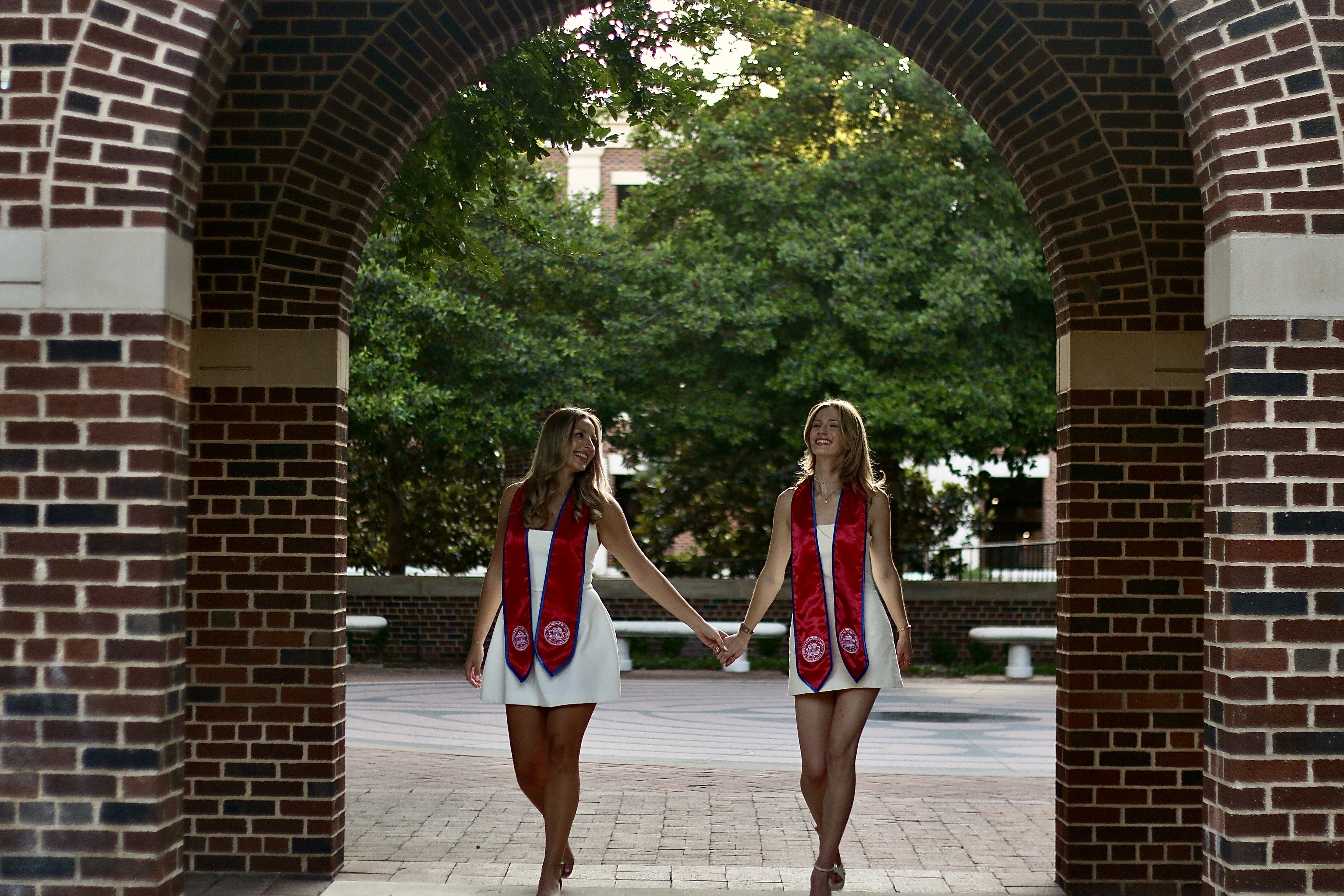 Two graduates walking through a brick arch