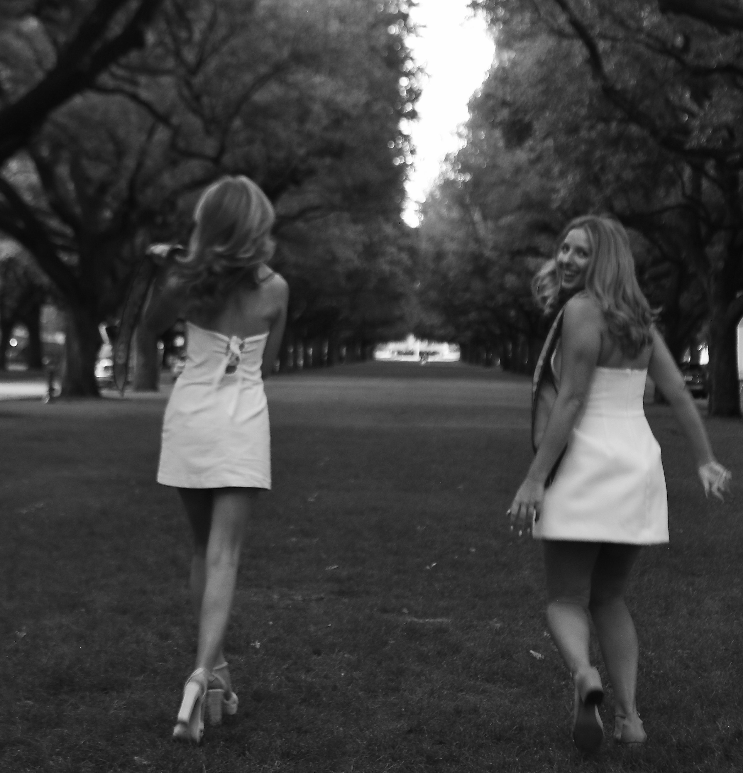 Two graduates walking through trees in black and white